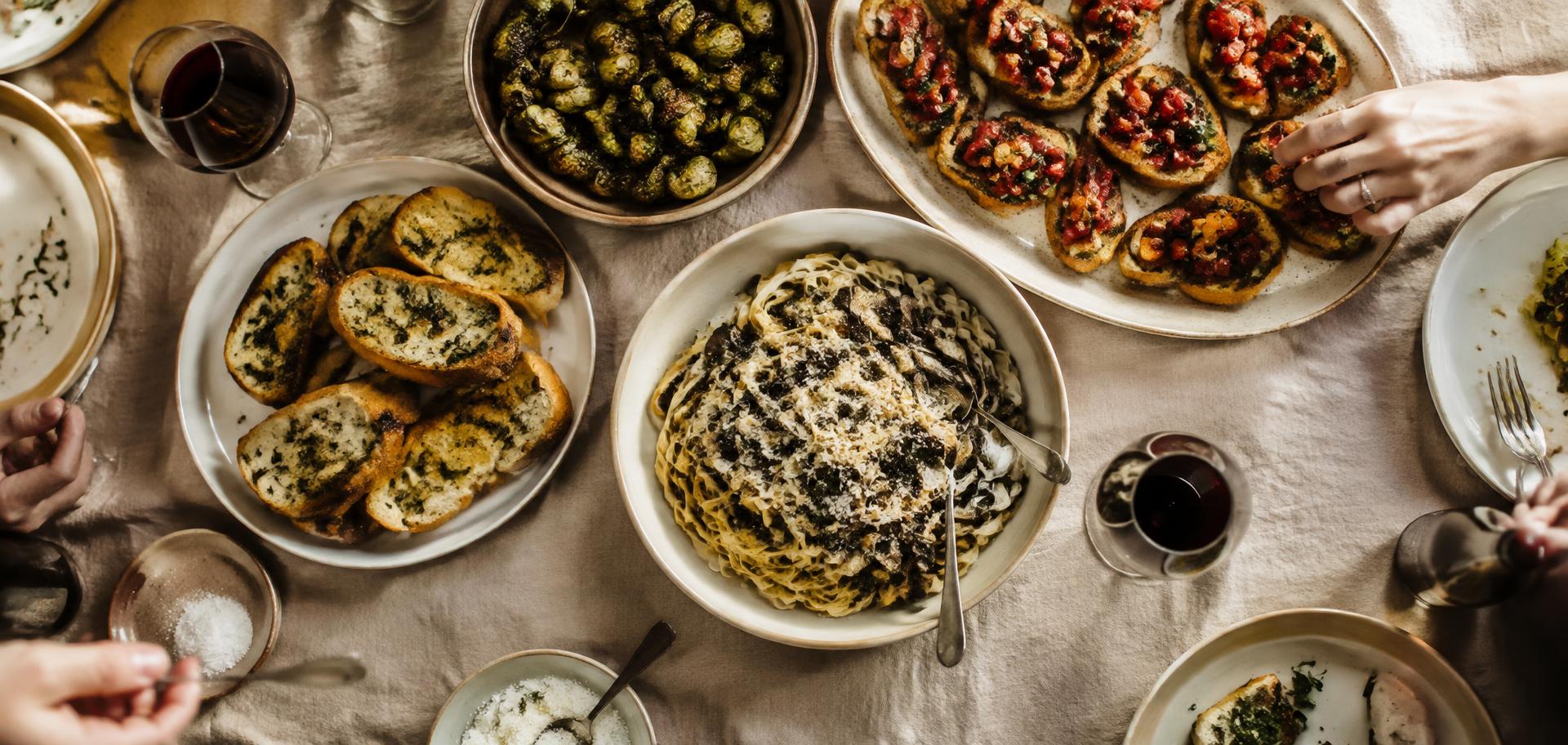 Overhead view of a shared table with bruschetta, Brussels sprouts, garlic bread, and mushroom pasta